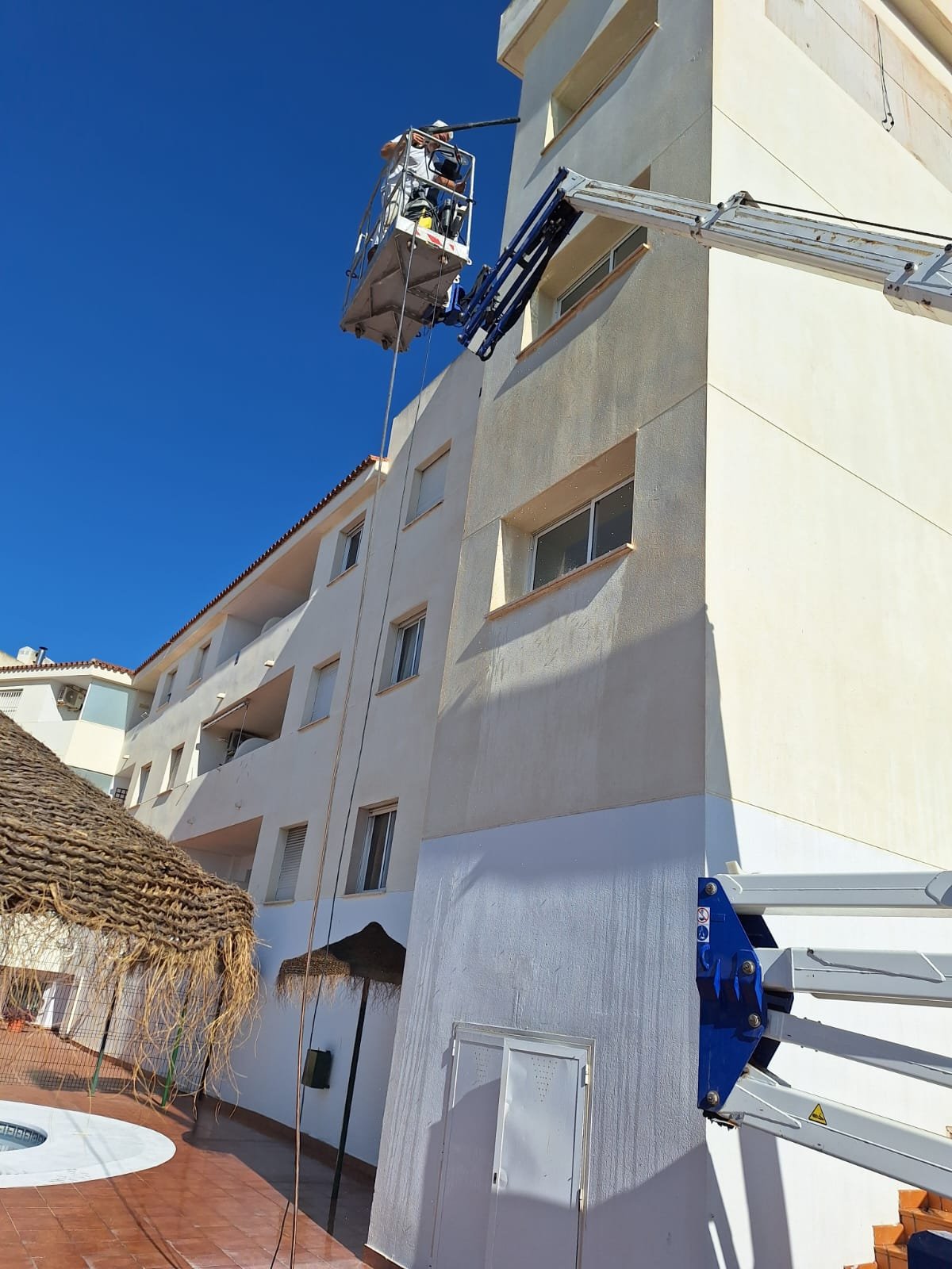 Plataforma elevadora trabajando en una fachada blanca de patio interior